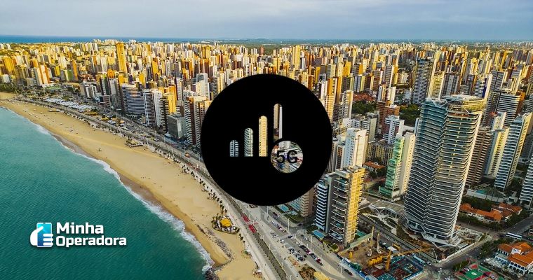 A imagem mostra uma vista aérea da orla de Fortaleza, no estado do Ceará, com prédios altos ao longo da costa, evidenciando o desenvolvimento urbano da região. O mar aparece à esquerda, contrastando com as construções modernas à direita. No centro da imagem, há um ícone preto circular com uma barra de sinal de celular e a inscrição 