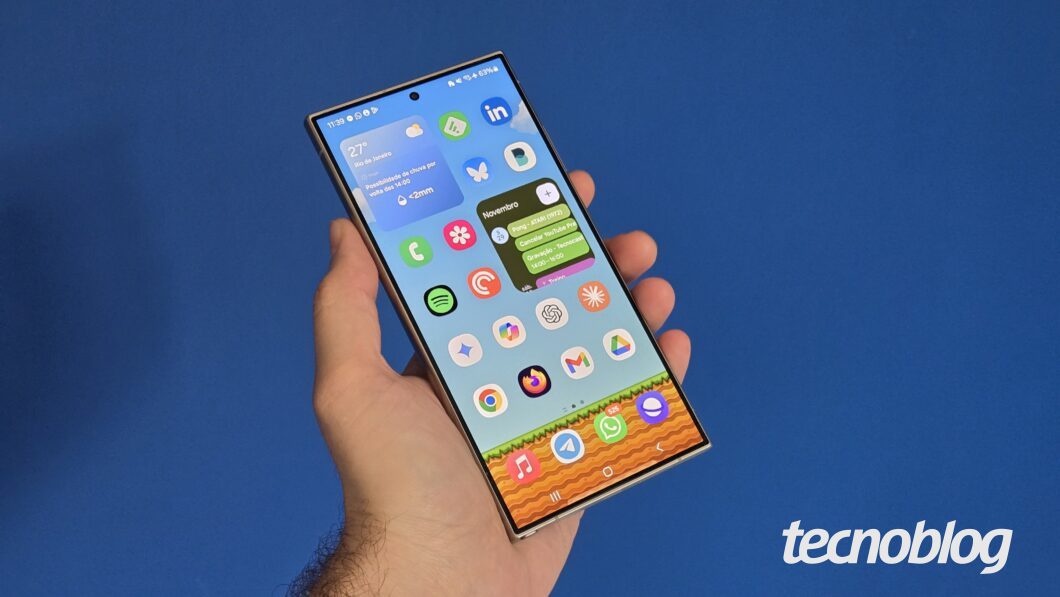 Mão segurando smartphone, visto de frente e mostrando a tela inicial