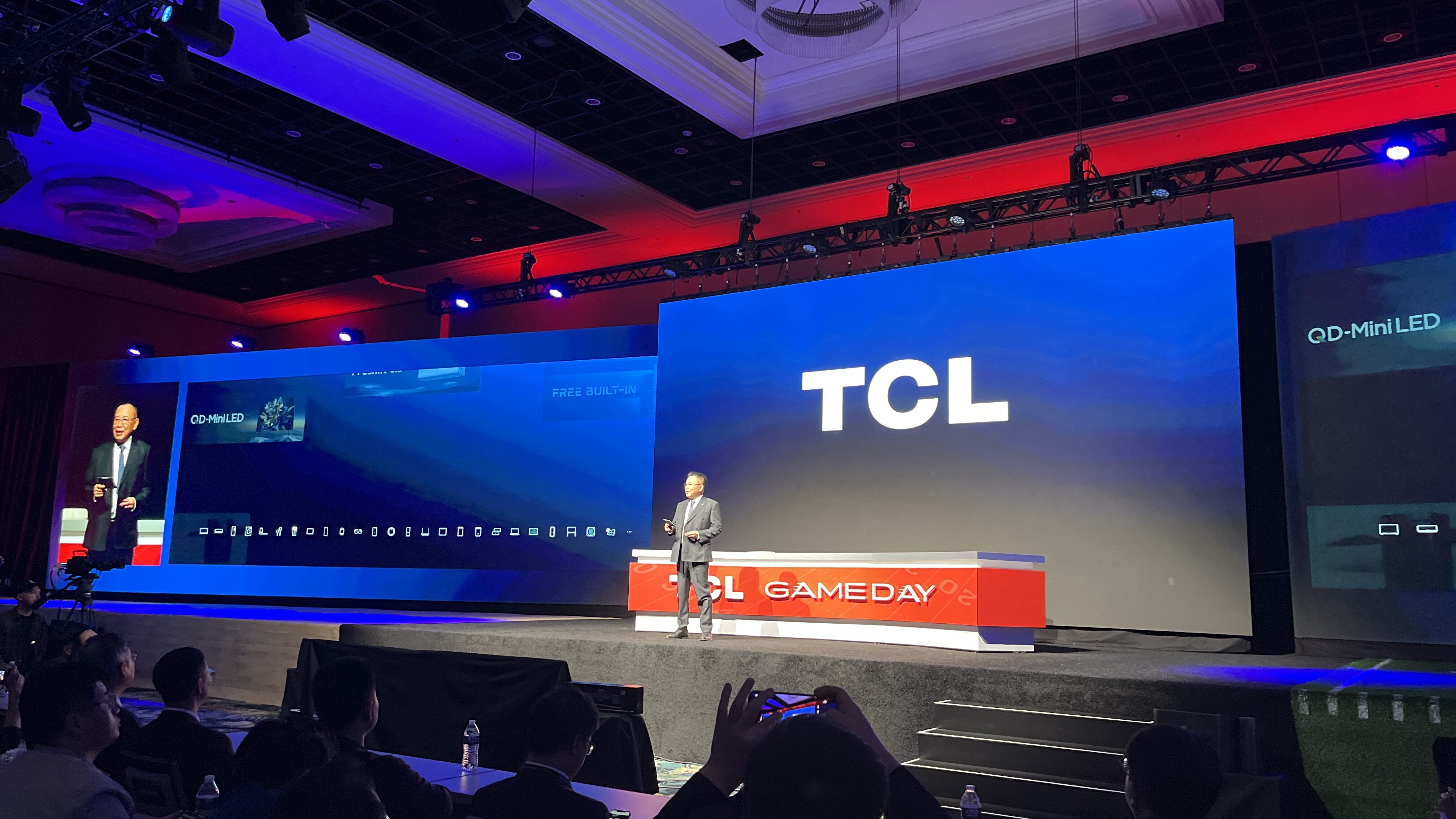 Li Dongsheng, homem asiático de terno, no palco da CES, diante de uma mesa e um telão com o logo da TCL